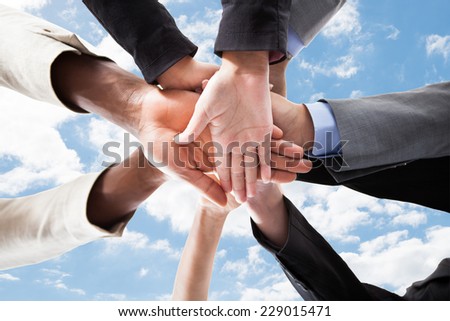 Closeup of multiethnic business people\'s hands on top of each other symbolizing unity against sky