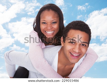 Portrait of happy young man giving piggyback ride to woman against sky