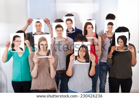 Group of multiethnic college students holding photographs in front of faces at classroom