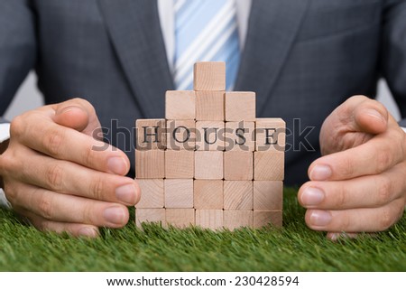 Midsection of businessman protecting house blocks on grass
