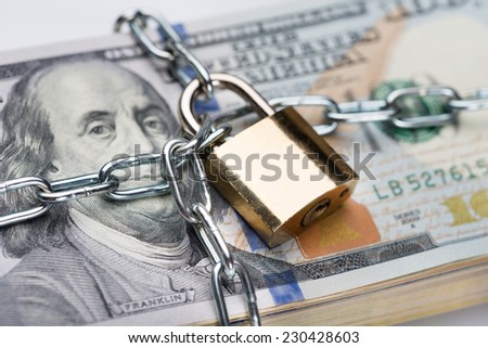 Closeup of metallic chain and padlock around dollar bundle