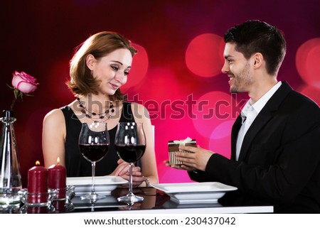 Loving man giving present to woman while having wine at restaurant table