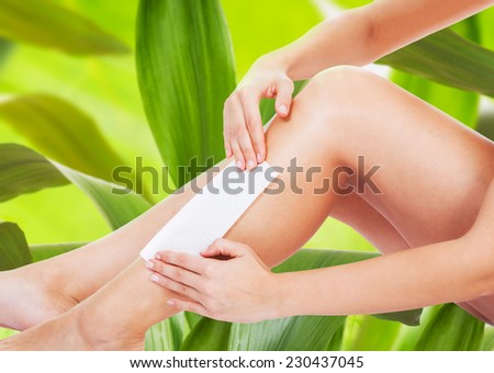 Low section of woman waxing leg against leaves