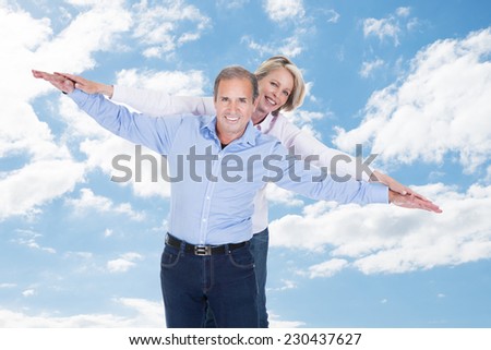 Portrait of happy couple with arms outstretched standing against cloudy sky