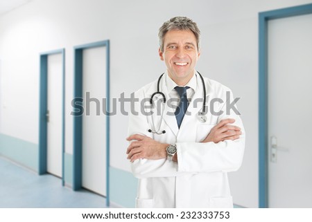 Portrait of happy senior doctor with arms crossed standing in hospital