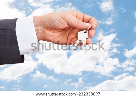 Closeup of real estate agent's hand holding keys against cloudy sky