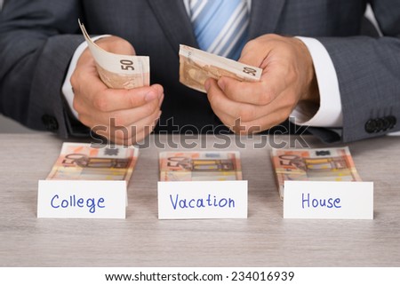 Midsection of businessman saving money for college; vacation and house at table