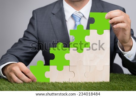 Midsection of businessman holding jigsaw graph on grass representing go green concept