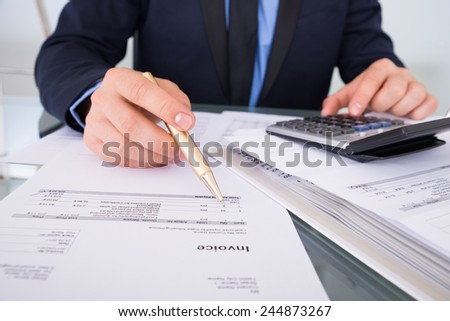Close-up Of Businessman Calculating Invoices Using Calculator