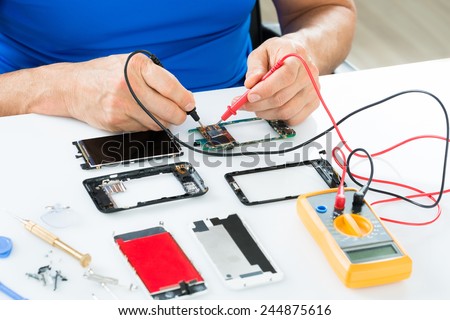 Close-up Of Man Repairing Cellphone With Multimeter