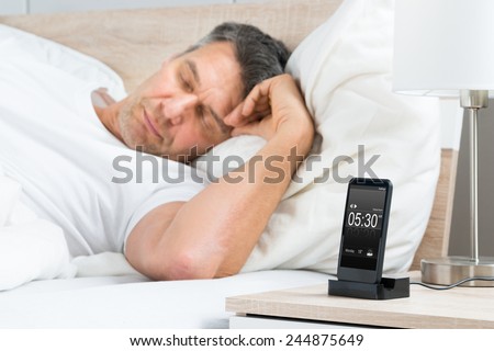 Mature Man Sleeping On Bed With Alarm On A Digital Cell Phone Display