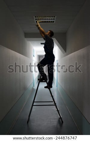Full length side view of electrician on stepladder installs lighting to the ceiling in office