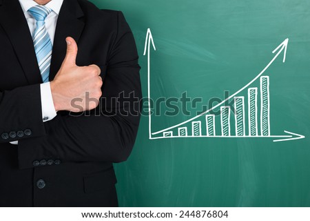 Midsection of young businessman showing thumbs up while standing by graph drawn on chalkboard
