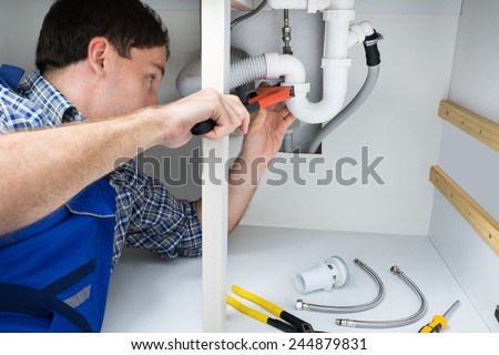 Portrait Of Male Plumber Fixing A Sink In Bathroom