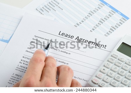 Close-up Of Person Hand With Pen And Calculator Over Lease Agreement