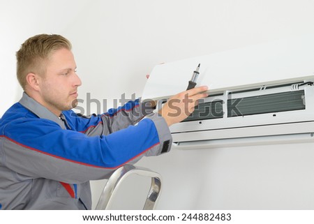 Young Man Repairing Air Conditioner Standing On Stepladder