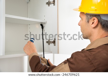 Close-up Of Pest Control Worker Wearing Hardhat Spraying Pesticides On White Shelf