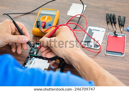 Close-up Of Technician Repairing Cellphone With Multimeter On Desk