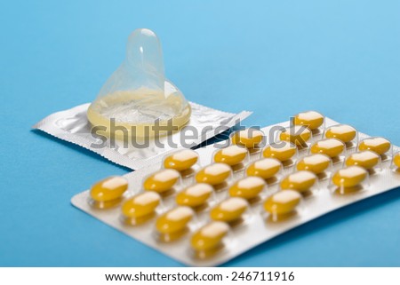 Close-up Of Birth Control Pills And Condom On Blue Background