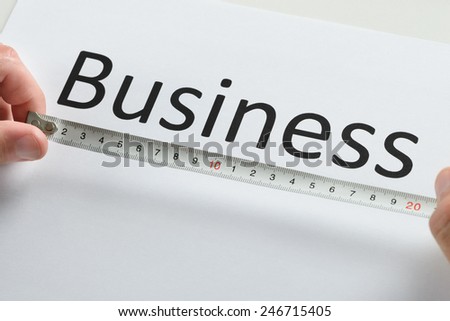 Close-up Of Person Hand Measuring The Text Business With Measure Tape