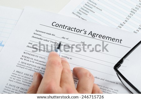 Close-up Of Hand With Pen And Eyeglasses Over Contractor Agreement