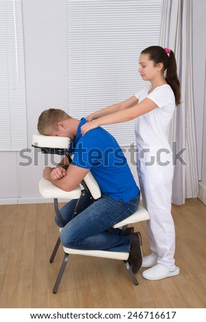 Female Physiotherapist Giving Shoulder Massage To Man On Massage Chair