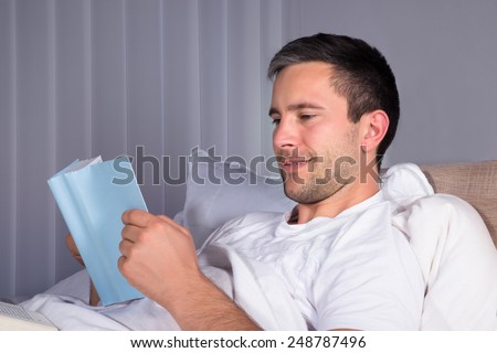 Close-up Of A Smiling Man On Bed Reading Book
