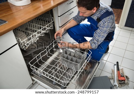 Portrait Of Male Technician Repairing Dishwasher In Kitchen