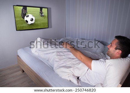 Portrait Of A Smiling Man Watching Football Match On Television In Bedroom