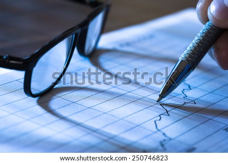 Pen In Hand Pointing At Graph On Paper With Glasses