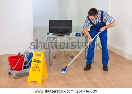 Portrait Of A Male Janitor Cleaning Office With Wet Floor Sign