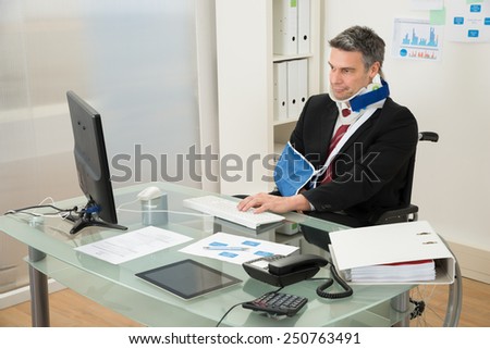 Portrait Of Disabled Mature Businessman On Wheelchair Using Computer At Office