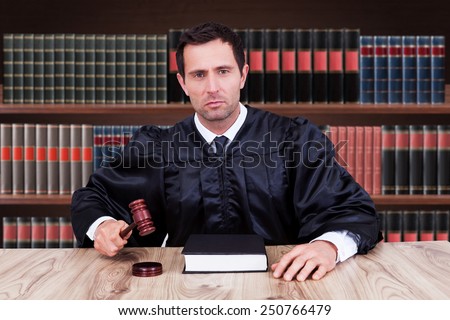 Portrait Of Serious Male Judge Striking Gavel In Courtroom