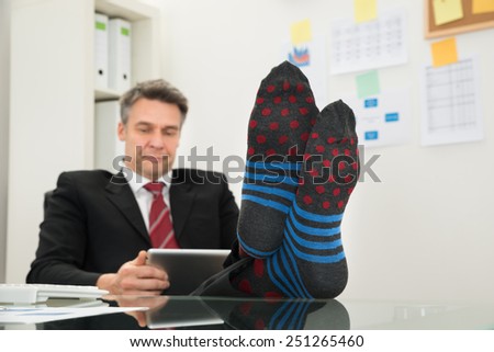 Portrait Of Mature Businessman With Socks In His Feet Using Digital Tablet At Office
