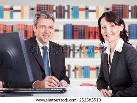 Two Happy Mature Businesspeople Sitting At Office Desk