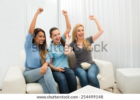 Multiethnic Women Sitting On Couch Cheering Watching Television