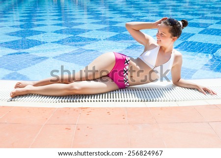 Full length portrait of happy young woman in swimwear relaxing at poolside