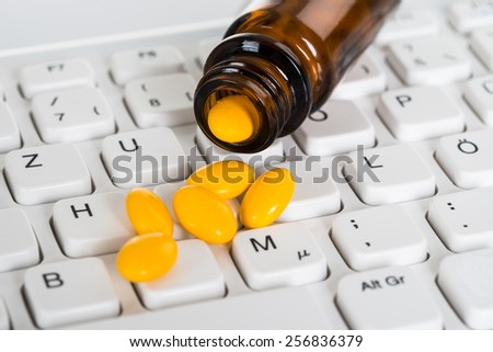 Close-up Of Pills Spilled From Bottle On Computer Keyboard