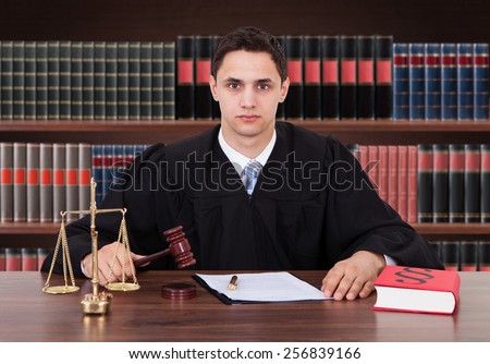 Portrait Of Young Male Judge Striking Gavel In Courtroom