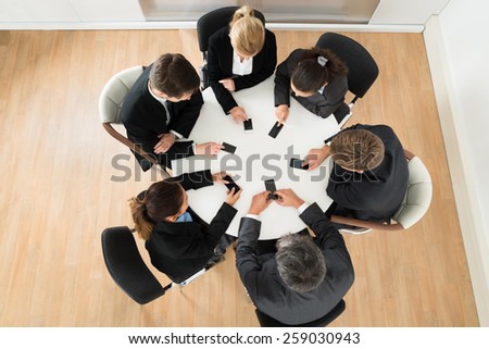 Group Of Businesspeople Using Cell Phone Sitting At Table