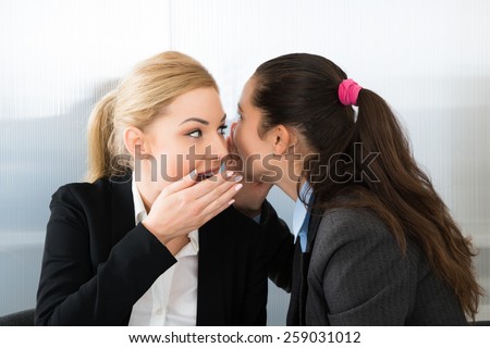 Businesswoman Whispering Into A Female Colleague Ear