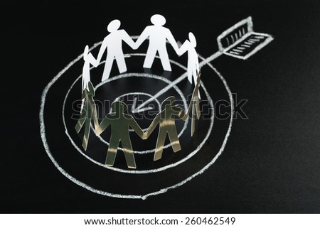 Circle Of White Paper Cut-out Figures Over Dart And Arrow Drawn On Blackboard With Chalk