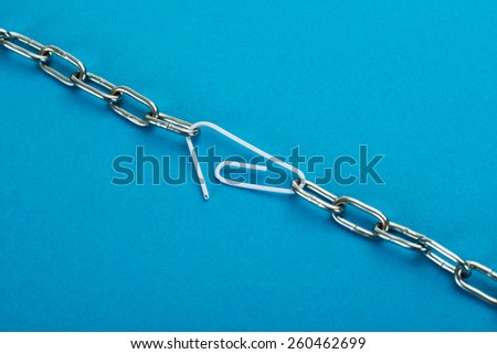 Close-up Of Metal Chain Linked With Paper Clip On Blue Background