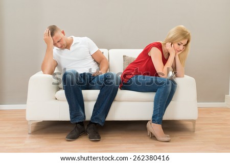 Depressed Young Couple Sitting On Sofa At Home