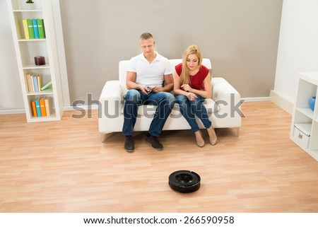 Young Couple Using Remote Control Toward Robotic Vacuum Cleaner