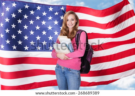 Portrait of happy female college student with backpack and books standing against white background