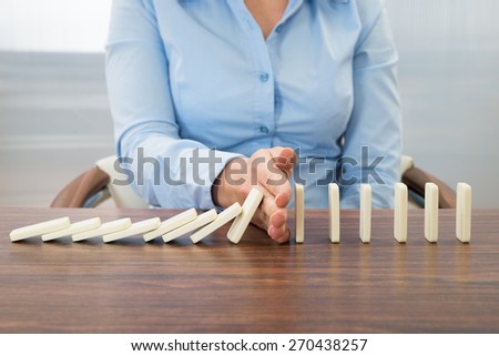 Close-up Of Businesswoman Stopping The Effect Of Domino With Hand At Desk