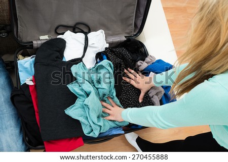 High Angle View Of Woman Packing Clothes In Suitcase