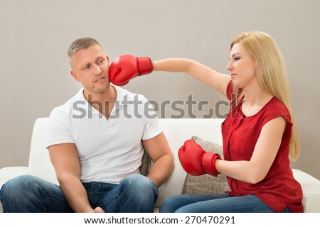 Portrait Of Young Couple Sitting On Sofa Fighting With Boxing Gloves