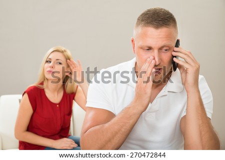 Wife With Curiosity Looking At Husband Talking Privately On Mobile Phone
